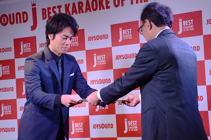 株式会社エクシング 代表取締役社長　吉田篤司より賞状とトロフィーを受け取る桐谷 健太さん